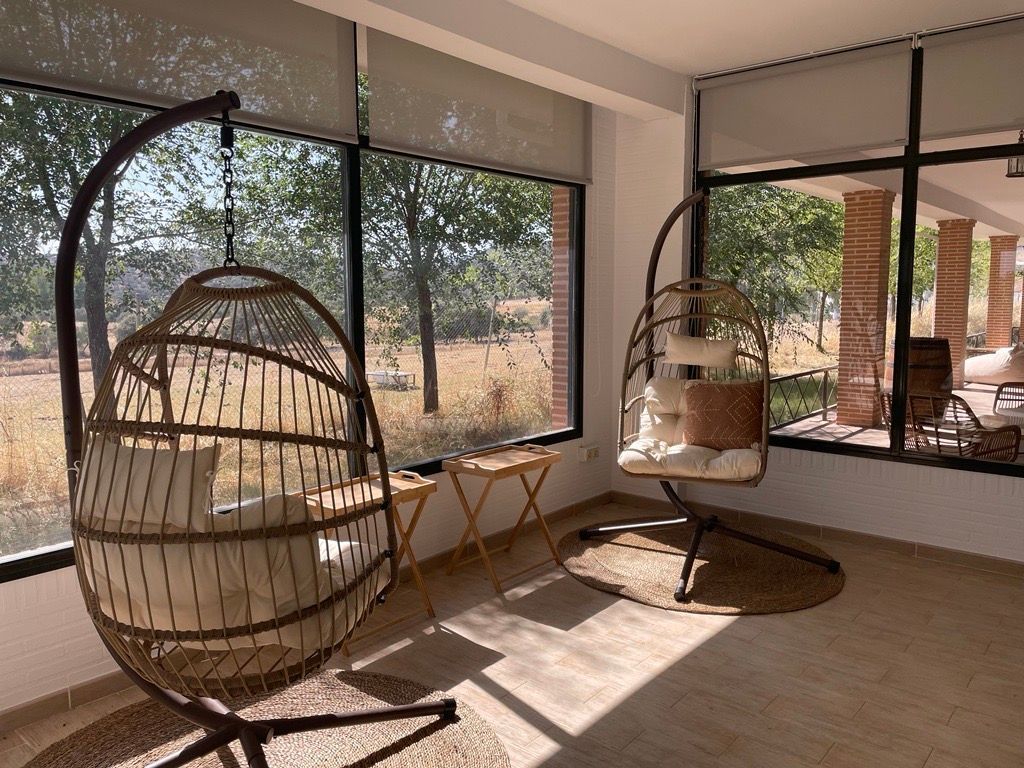Bright coworking sunroom with hanging rattan chairs and panoramic windows looking onto the dehesa countryside.