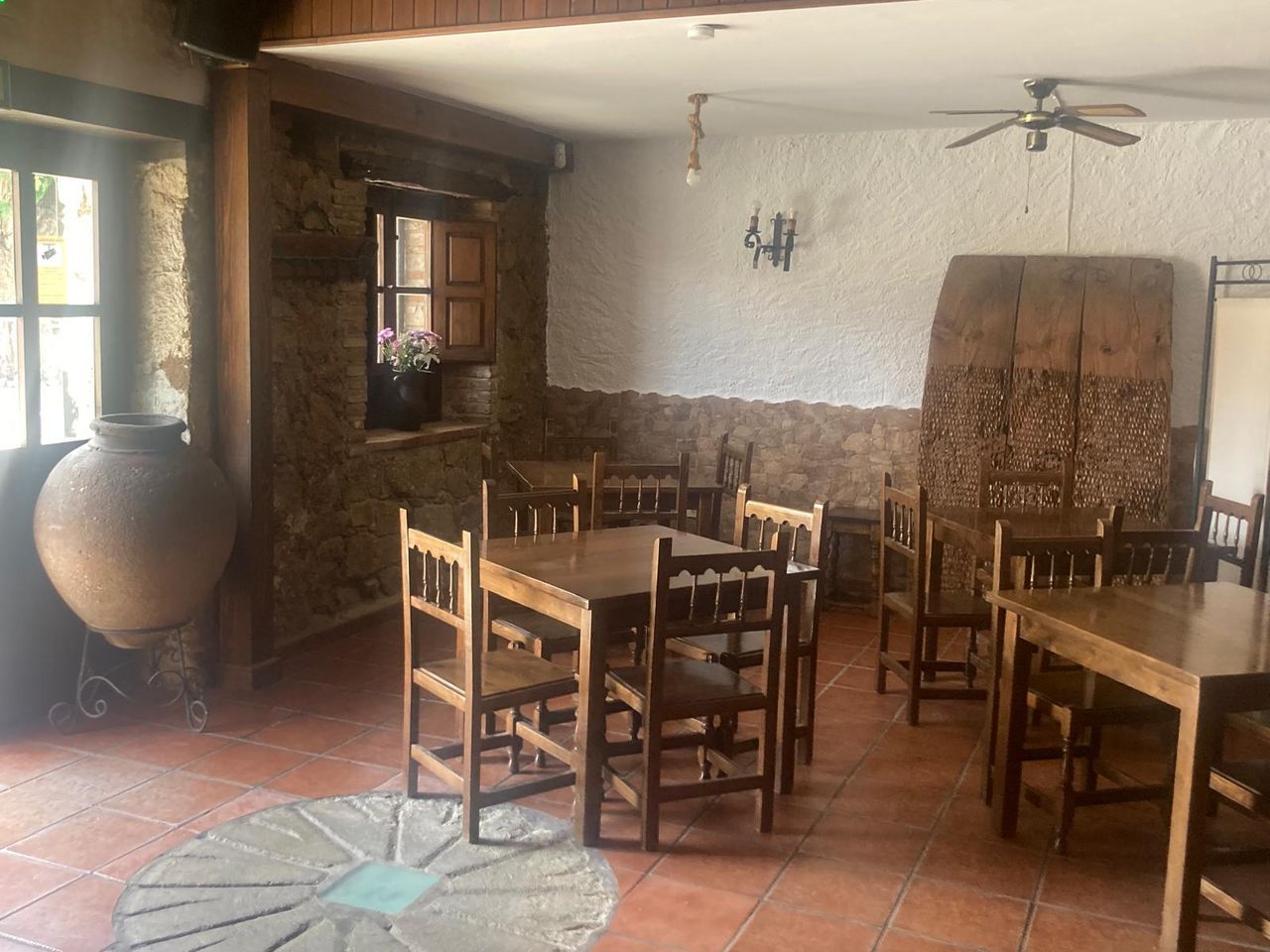 The stone dining room with its clay tinaja, a millstone set into the floor and wooden tables laid out
